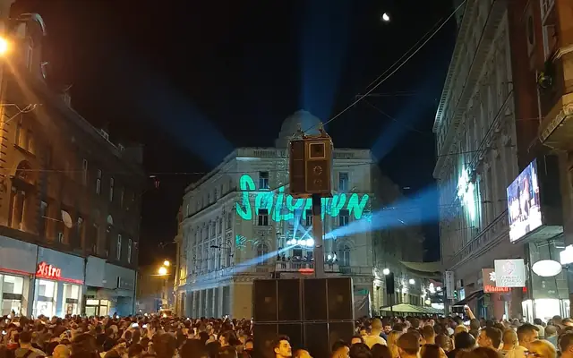 השם SOLOMUN מוקרן על בניין בסרייבו, לייזרים מעל קהל שממלא את הרחוב, 2019